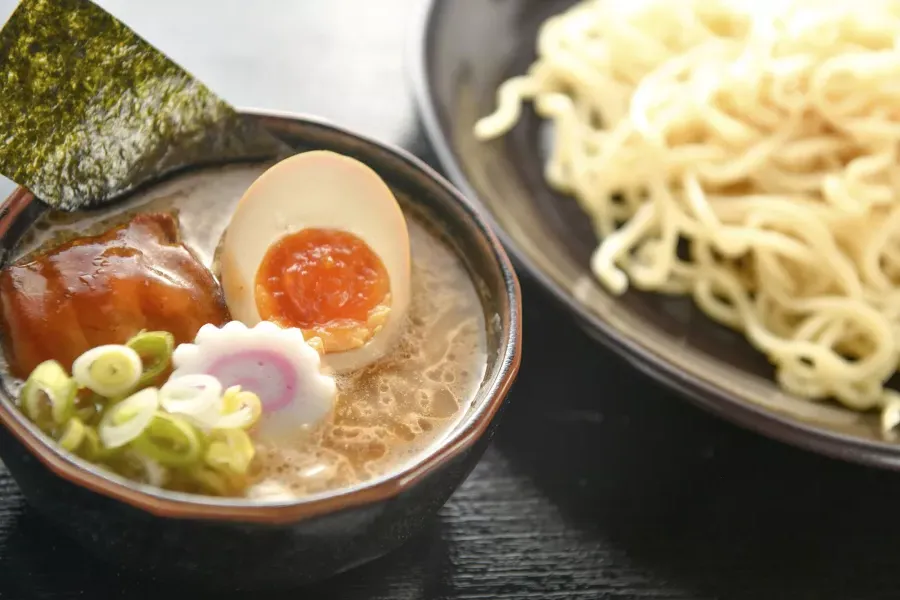 Gros plan d'un bol de nouilles et d'un bol de soupe ramen avec un œuf poché, coupé en deux.